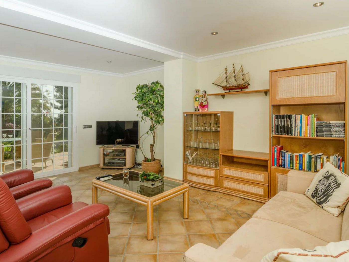 Living area featuring terracotta tile flooring, red leather recliners, and wooden cabinetry. Large sliding glass doors provide natural light and terrace access.