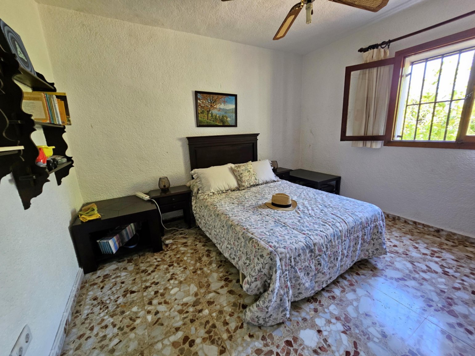 Bedroom featuring traditional terrazzo flooring, a dark wood headboard, and a window with wooden frames providing ample natural illumination.