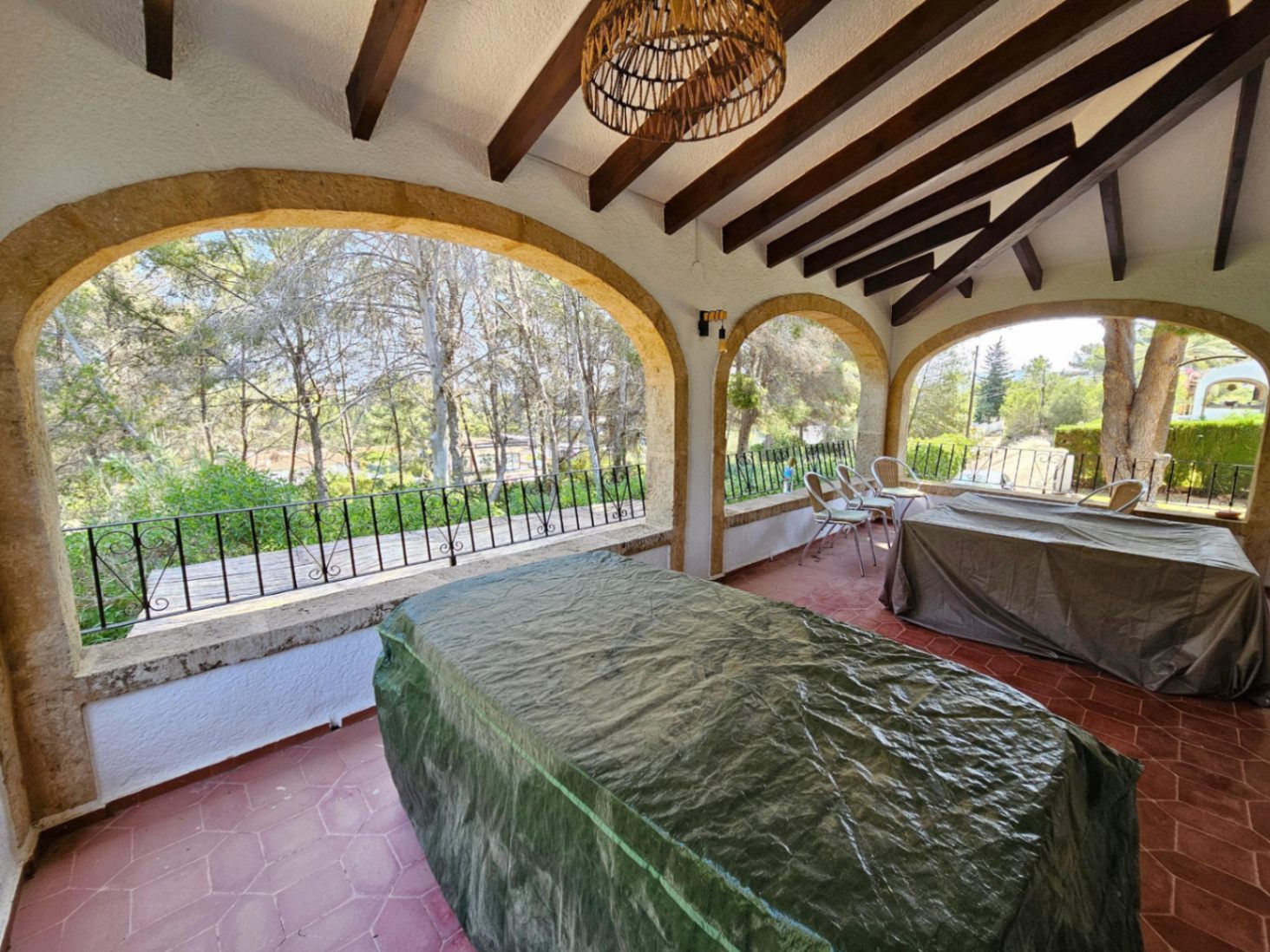 Covered terrace featuring traditional stone arches, dark wooden ceiling beams, and terracotta flooring with views of the surrounding pine forest.