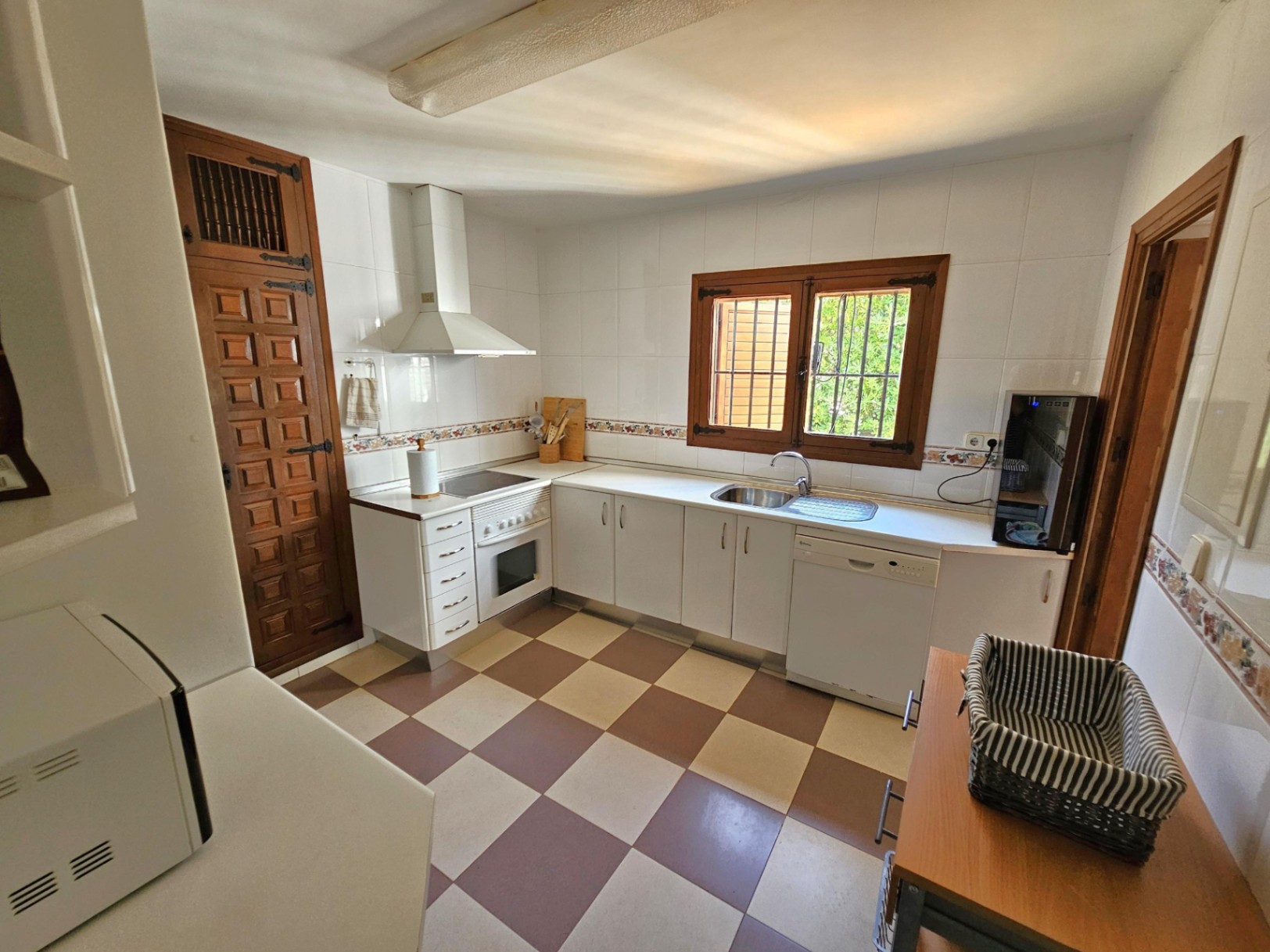 Kitchen featuring white cabinetry, checkered tile flooring, and rustic dark wood accents on the window and door. Includes a white oven and dishwasher.