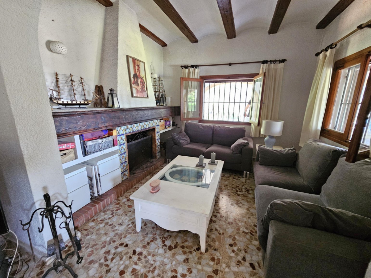 Living area featuring exposed wooden ceiling beams, a rustic fireplace with decorative tiles, and traditional terrazzo flooring.