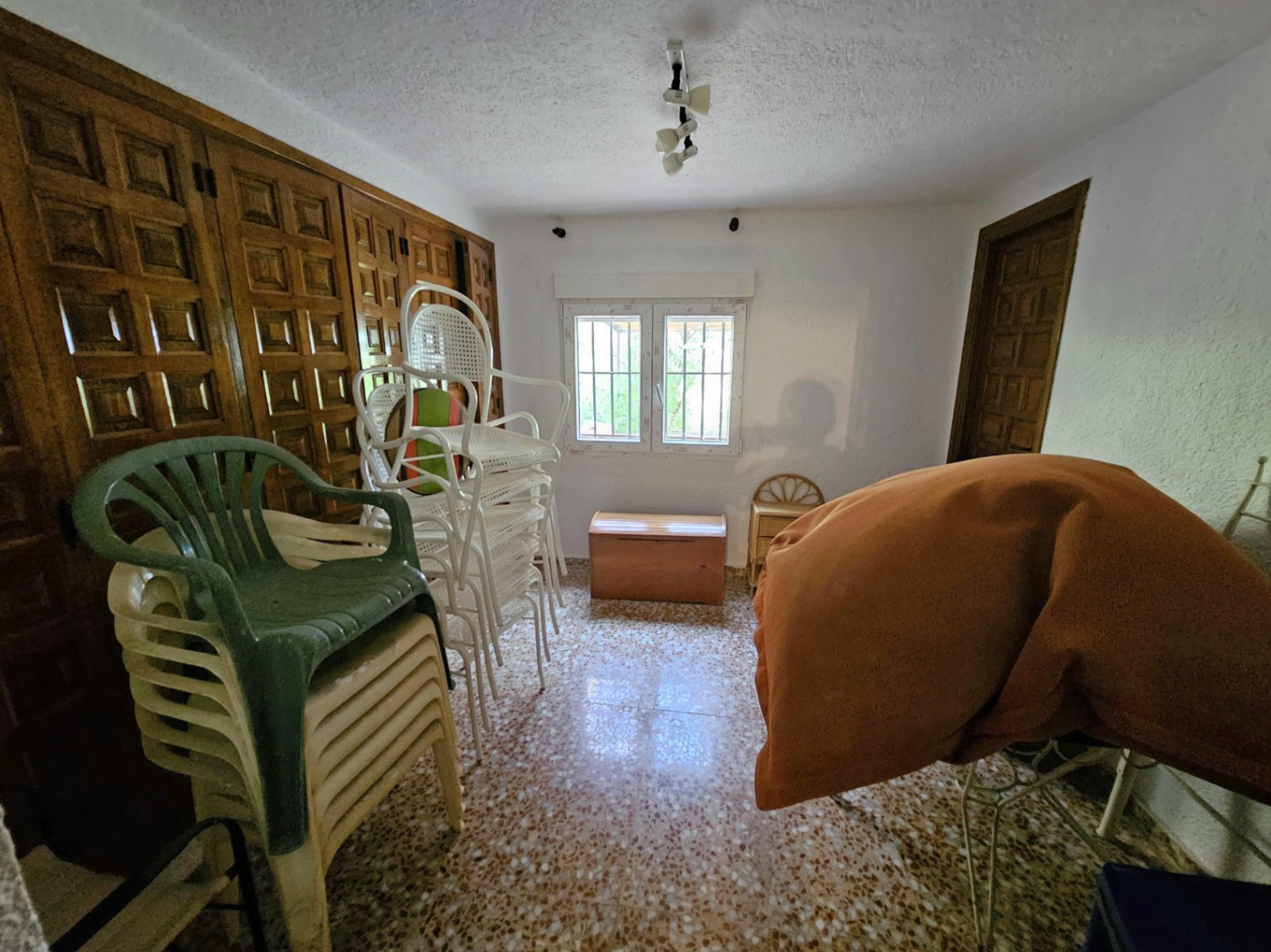 Room featuring built-in wooden wardrobes with paneled doors, terrazzo flooring, and a window with security bars. Functional space for storage.
