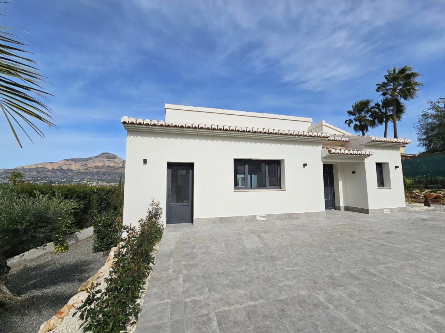 Exterior view of the villa featuring a white facade, roof tiles and gray paved access.