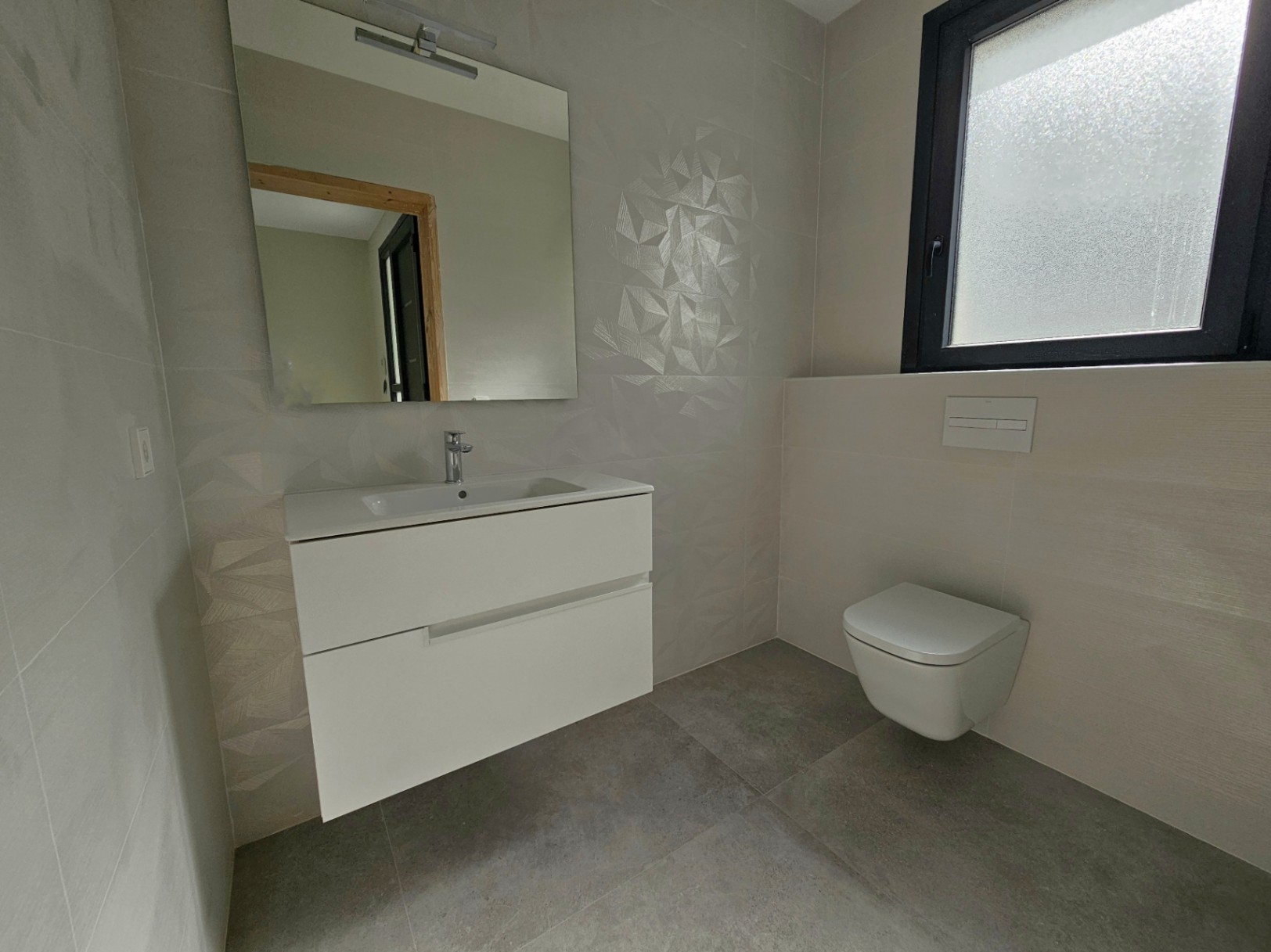 Modern bathroom detail with a floating white vanity, toilet, and geometric patterned tiles.