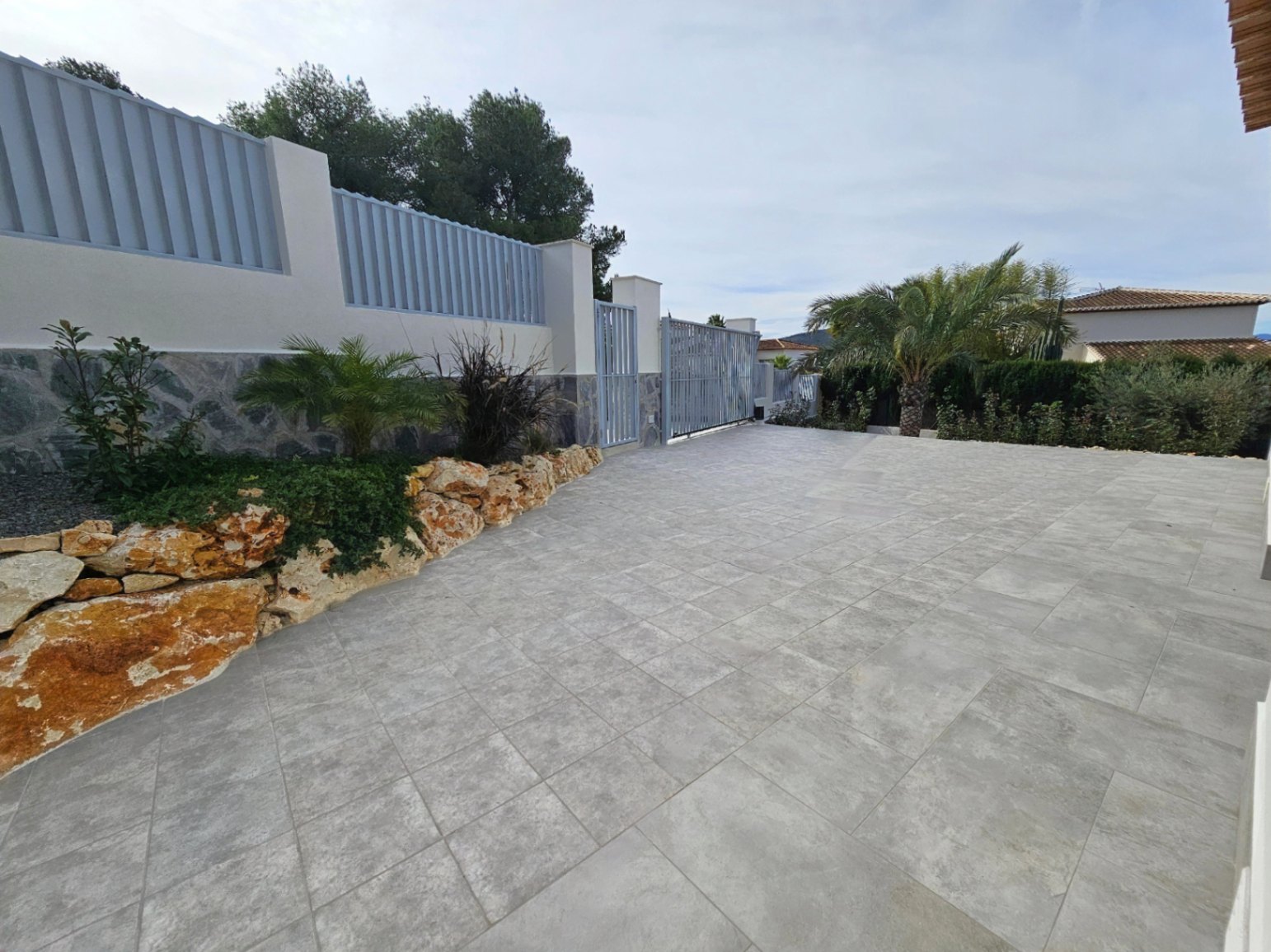 Paved driveway with gray security gate and rock garden featuring Mediterranean plants.