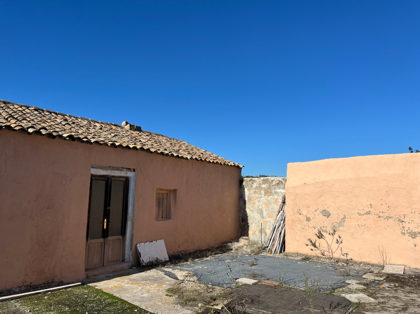 Exterior view of a traditional finca featuring a terracotta facade, clay tile roofing, and a wooden entrance door, set against a clear blue sky.