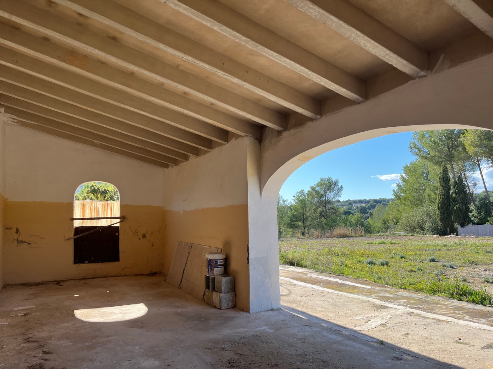 Porch under renovation featuring an exposed beam ceiling and a large archway overlooking the surrounding countryside and pine trees.