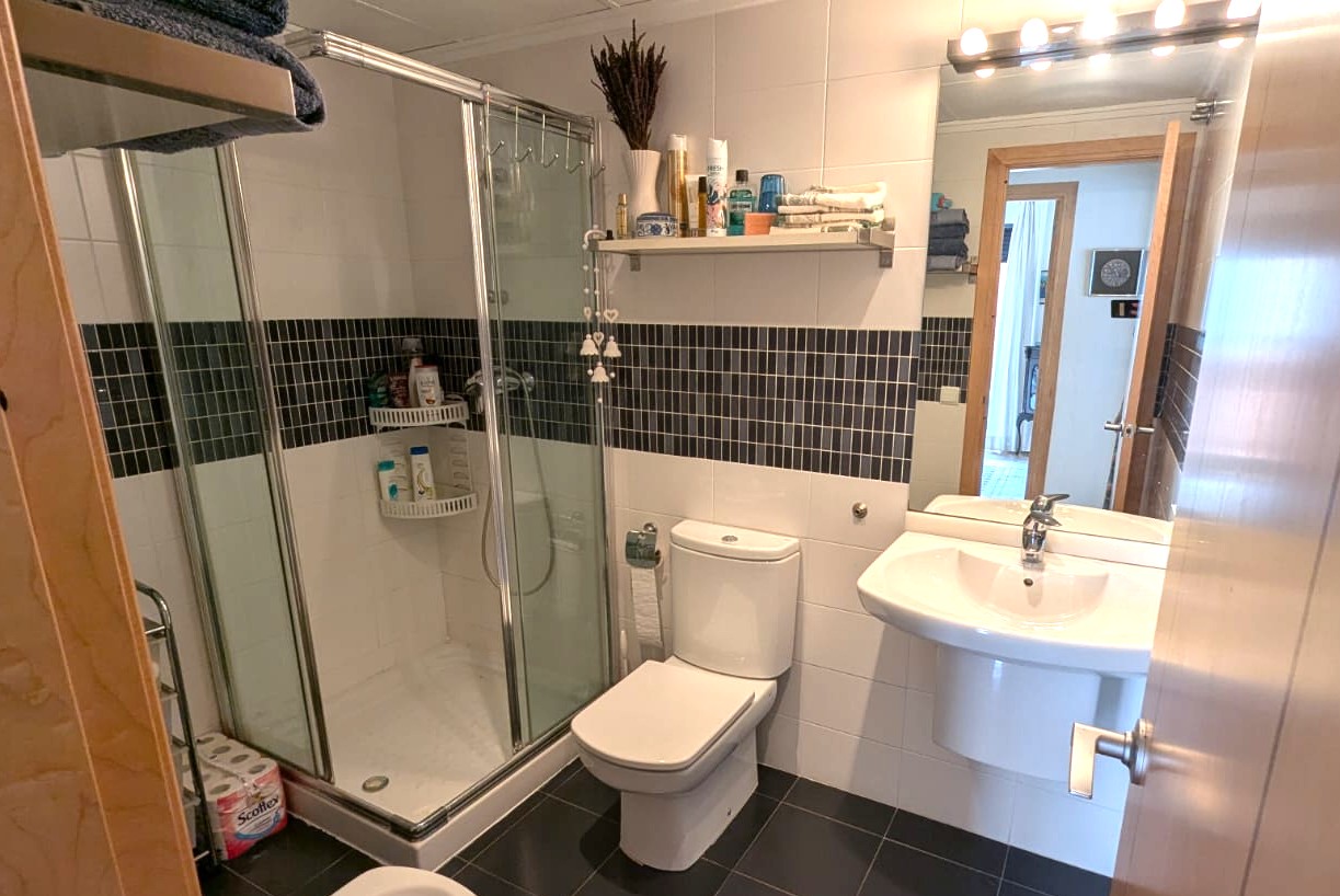 Bathroom featuring a glass shower enclosure, white ceramic wall tiles with a dark mosaic border, and dark grey floor tiling.