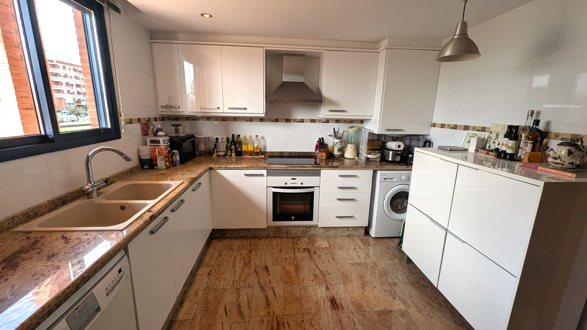 Functional kitchen featuring white cabinetry, granite countertops, and natural stone flooring. Includes integrated appliances and a window with dark framing.