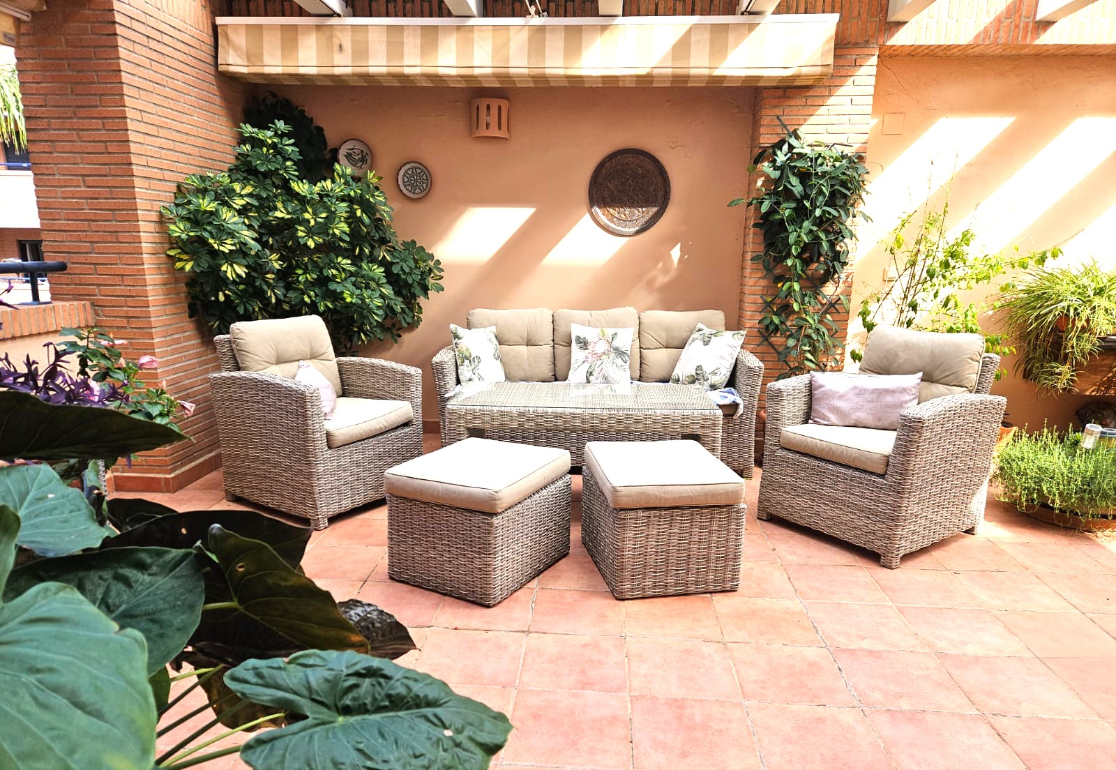 Private terrace featuring terracotta tile flooring, a grey wicker lounge set with beige cushions, and a retractable awning set against exposed brick pillars.