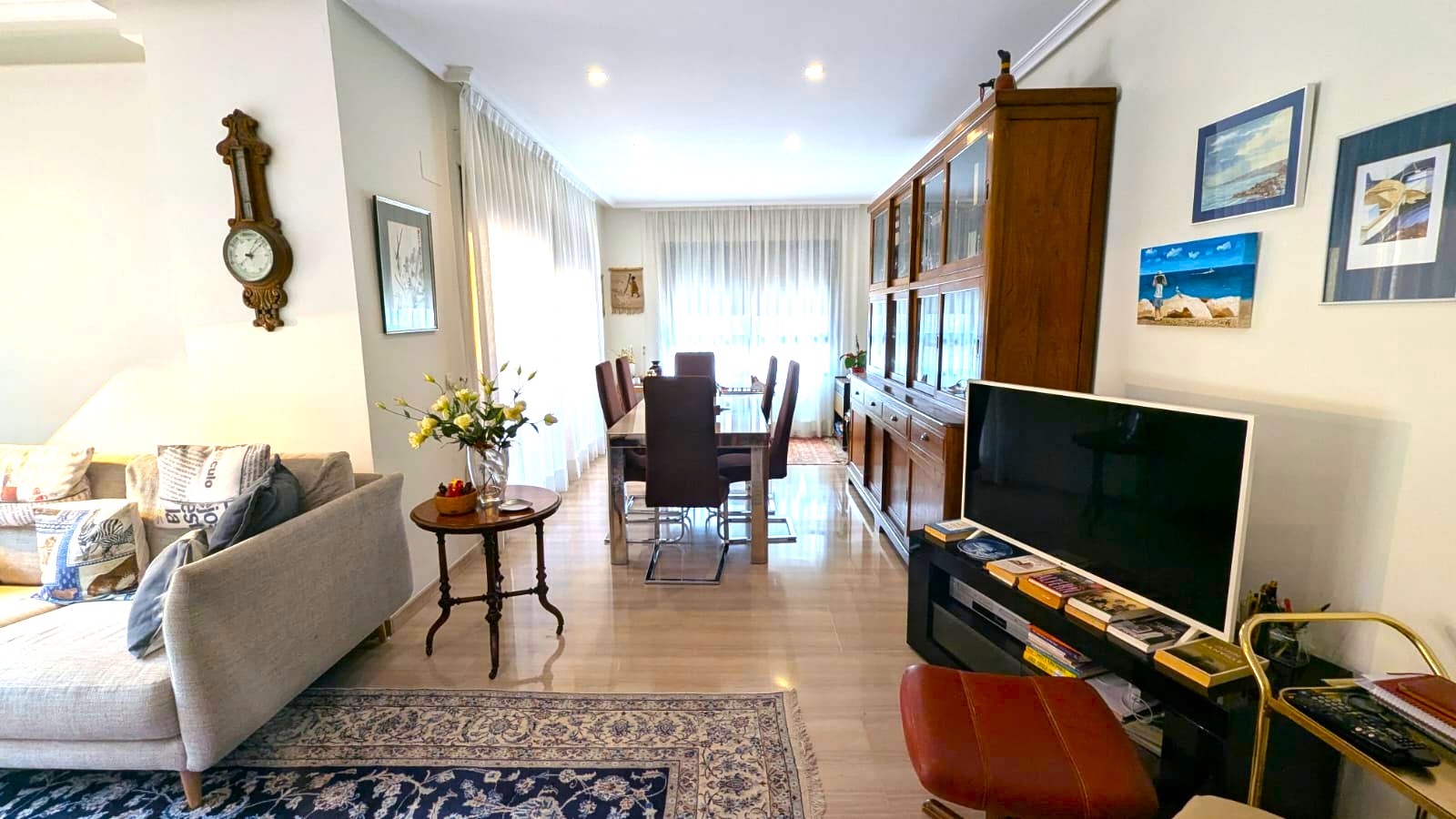 Spacious living-dining area featuring polished marble floors, a large wooden display cabinet, and a glass-top dining table under recessed ceiling lighting.