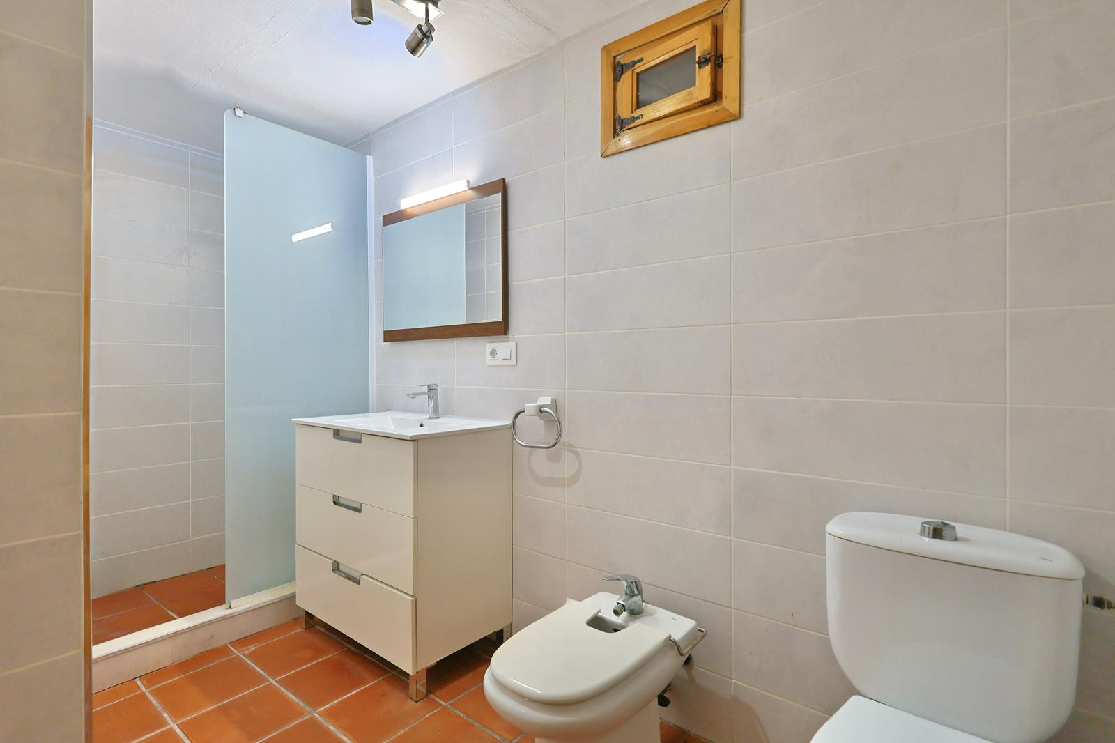 Bathroom featuring terracotta floor tiles, a white three-drawer vanity, bidet, and a walk-in shower with a frosted glass partition.