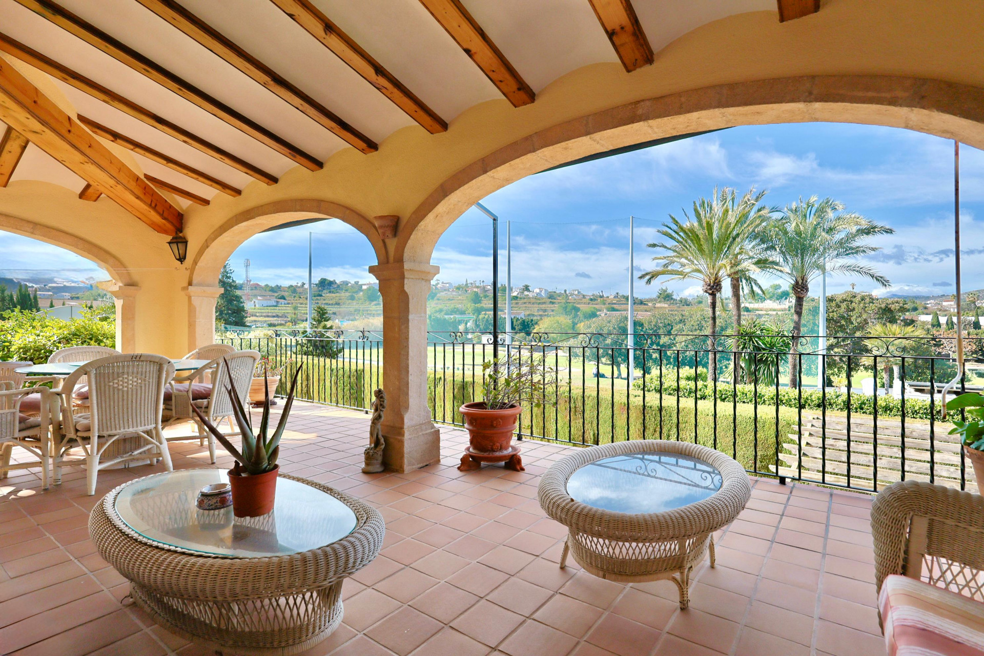 Covered terrace featuring traditional stone arches, exposed wooden beams, and terracotta tiling with panoramic views of the golf course and palm trees.