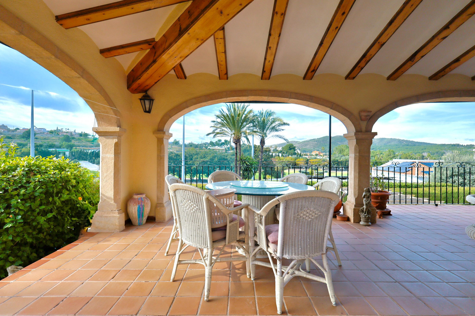 Covered terrace featuring traditional Tosca stone arches and wooden beams. Includes a dining area with wicker furniture and open views of the Jávea countryside.