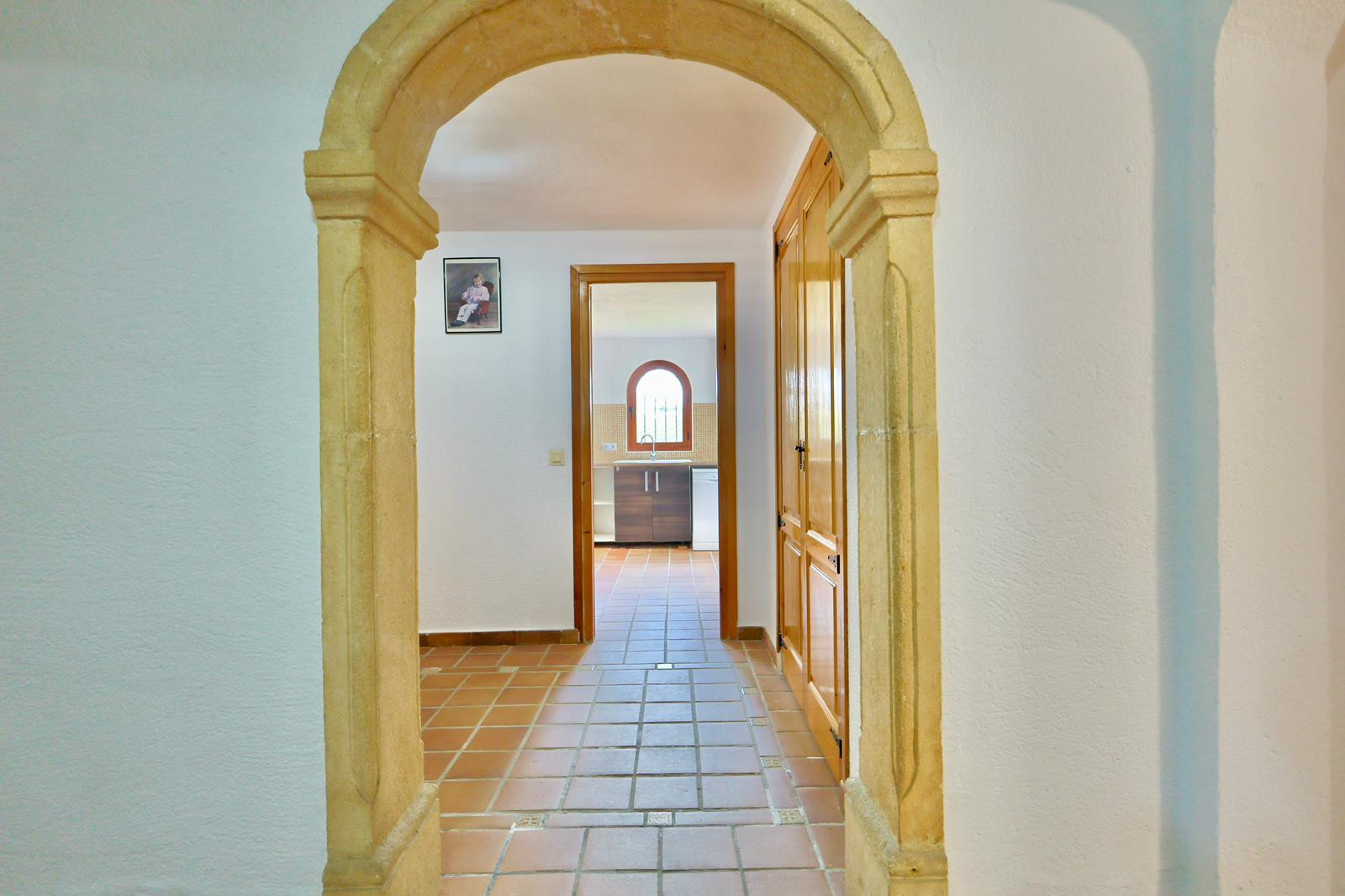 Entrance hallway featuring a traditional Tosca stone arch, terracotta tile flooring, and built-in wooden wardrobes leading toward the kitchen area.