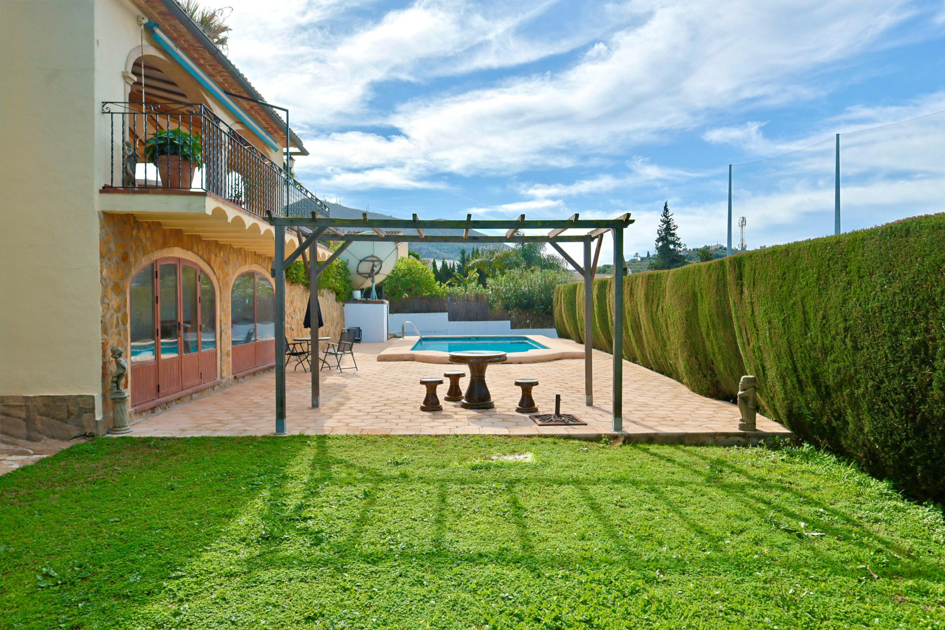 Exterior terrace with a wooden pergola and stone seating, adjacent to a private pool and lawn, featuring a stone-clad facade with arched windows.