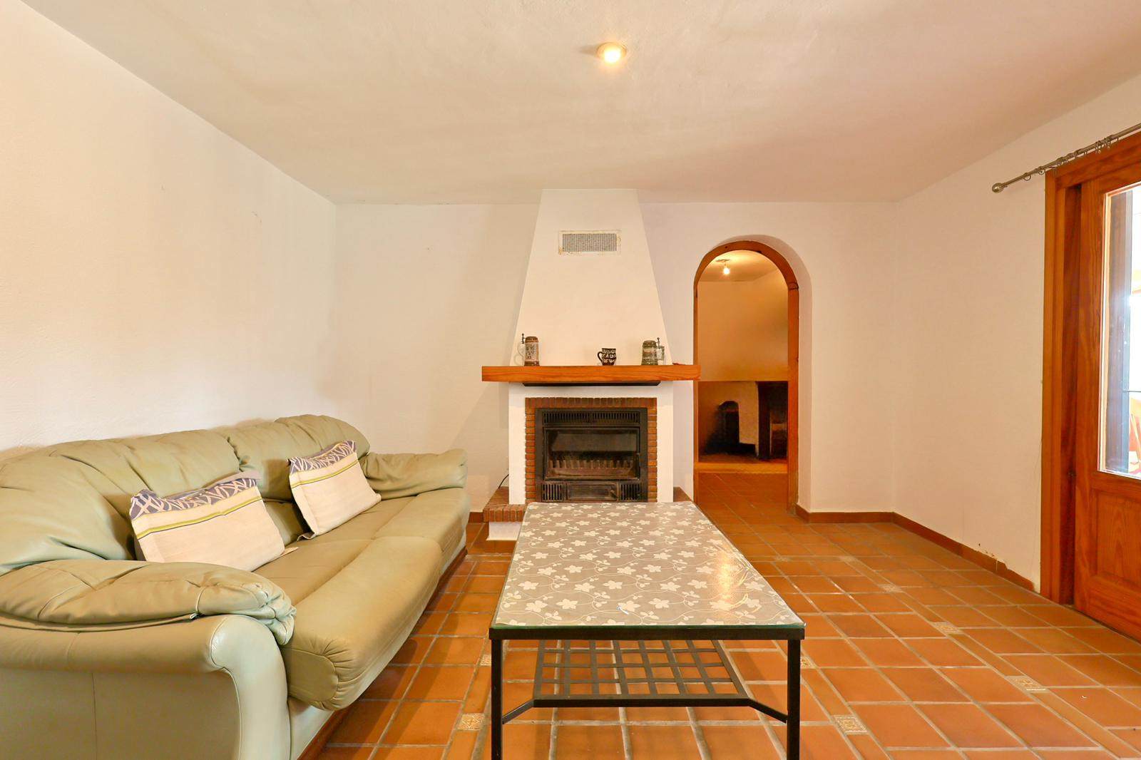 Living area featuring a built-in fireplace with a wooden mantel, terracotta tile flooring, and an arched doorway leading to adjacent rooms.