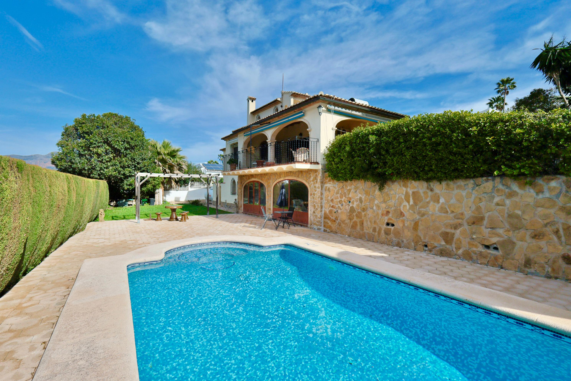 Mediterranean villa exterior featuring a private swimming pool, stone-clad lower facade, and arched terraces. Includes a paved sun deck and landscaped garden.