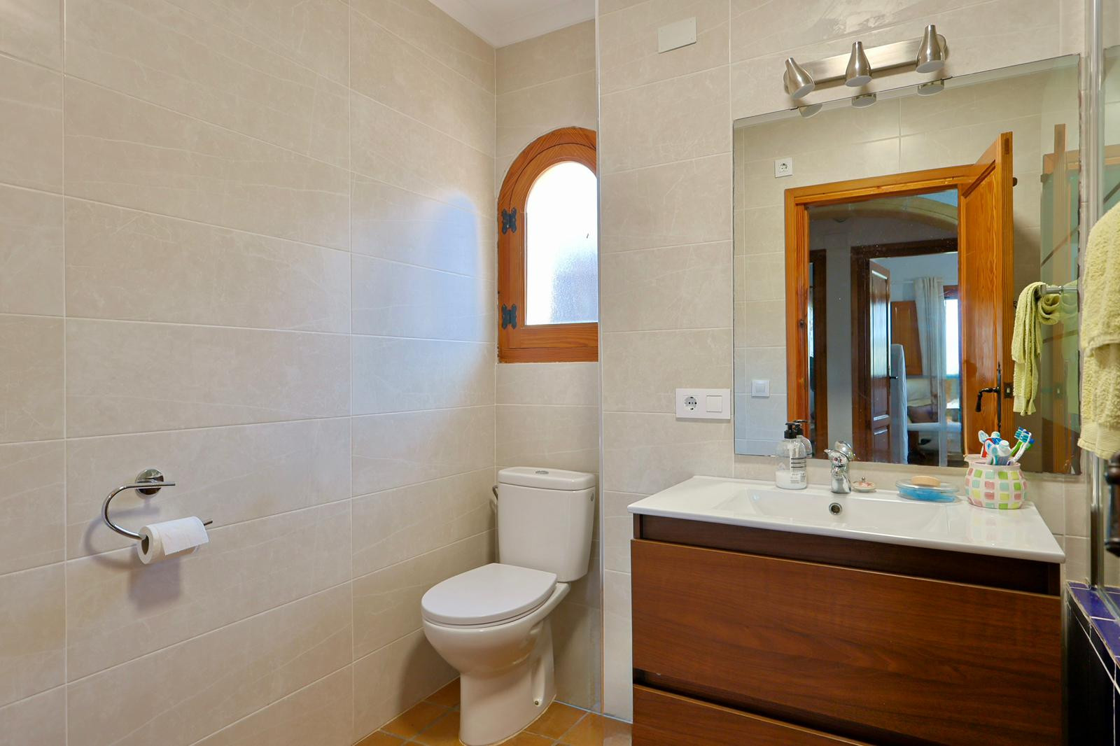 Modern bathroom featuring a dark wood vanity, integrated white sink, and a distinctive arched wooden window with neutral beige wall tiling.