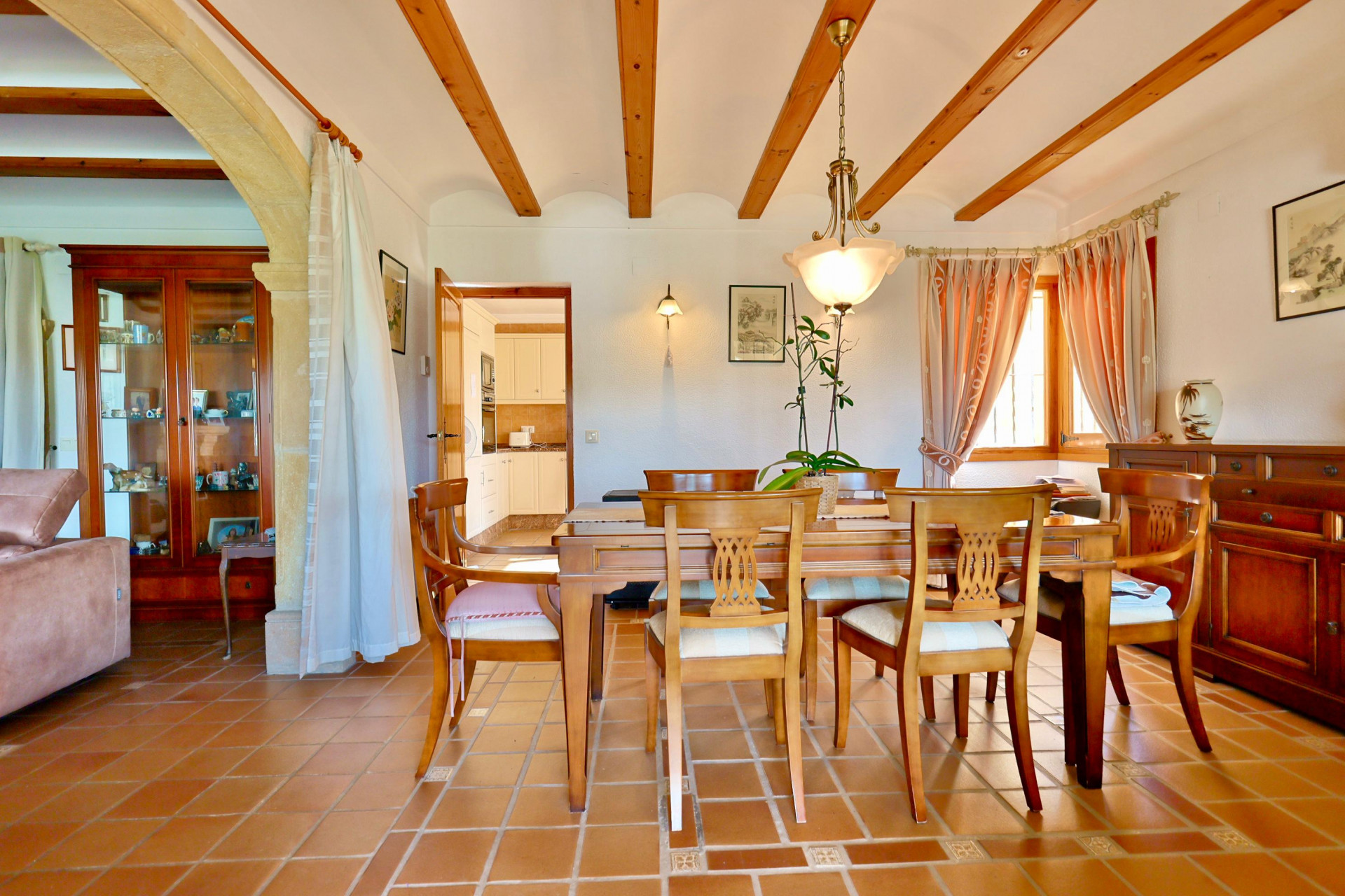 Rustic dining area featuring exposed wooden ceiling beams, terracotta tile flooring, and a traditional Tosca stone archway connecting to the living space.