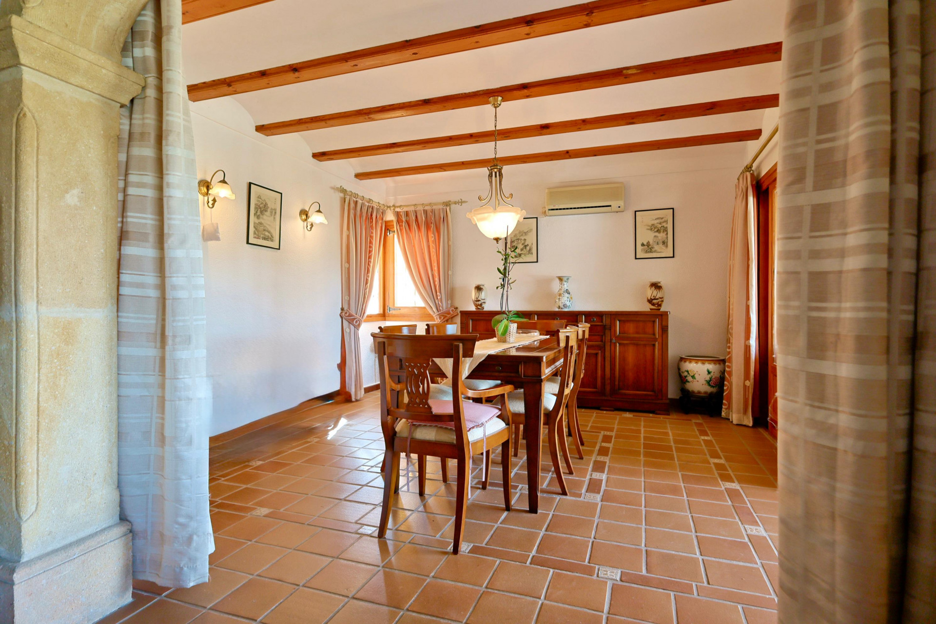 Traditional dining area featuring exposed wooden ceiling beams, terracotta tile flooring, and a Tosca stone archway. Furnished with a classic solid wood set.