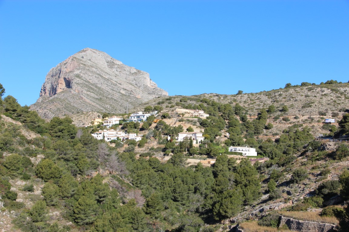Panoramic view of the La Corona hillside in Jávea, featuring Mediterranean vegetation and white villas set against the iconic Montgó mountain.