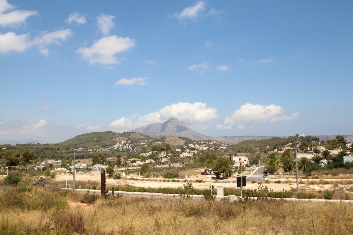 View of building plots with Montgó in the background, under a blue sky with scattered clouds.