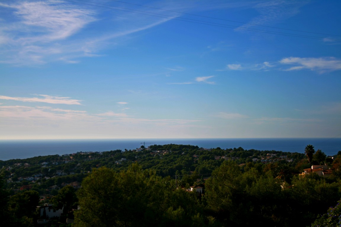 Panoramic view of Benimeit, Moraira, featuring the Mediterranean Sea in the background and a blue, cloudy sky.