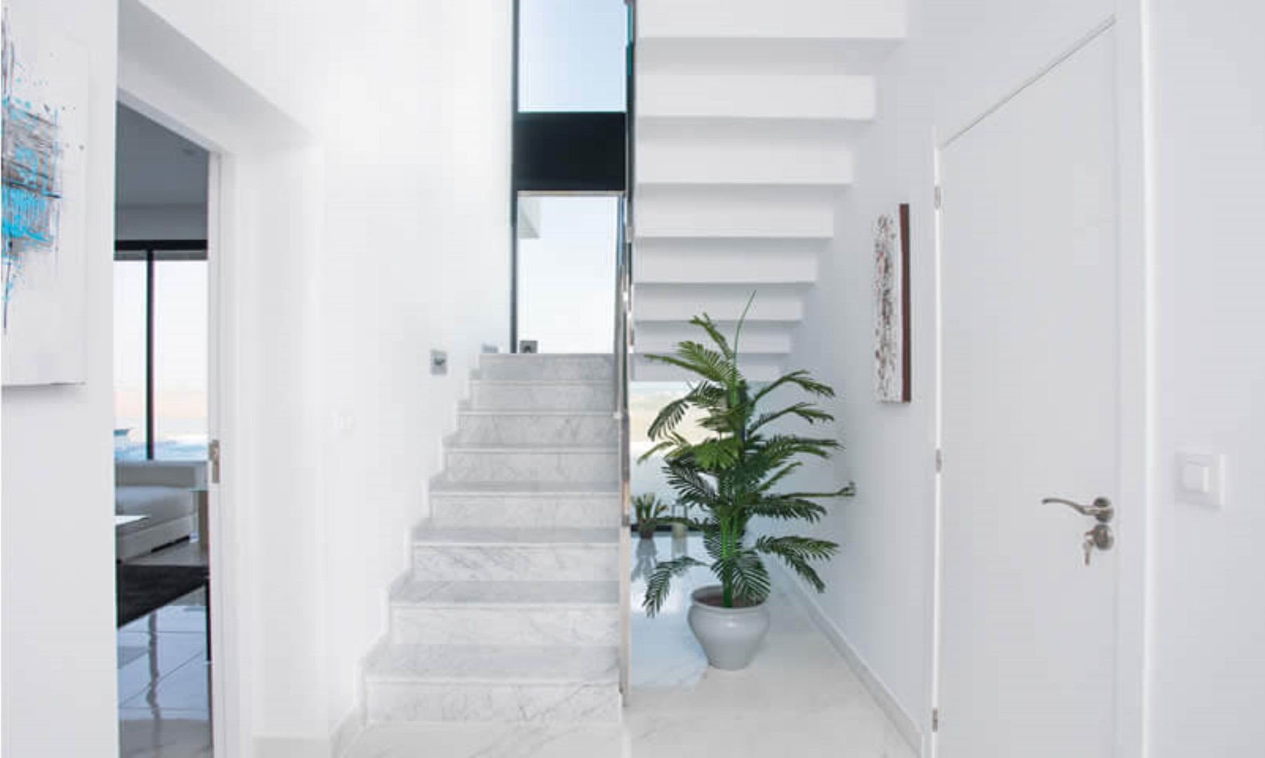Minimalist entrance hall featuring a marble staircase with white floating steps, illuminated by a tall vertical window providing natural light.