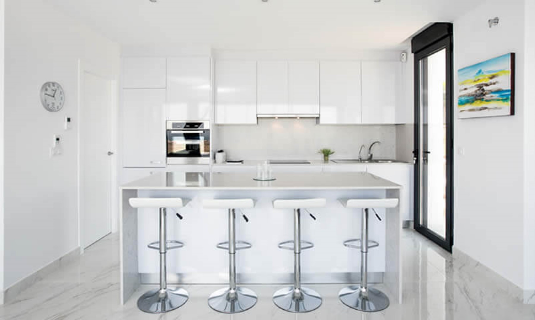 Modern open-plan kitchen featuring high-gloss white cabinetry, a central island with quartz countertop, and four bar stools. Marble-effect porcelain flooring throughout.