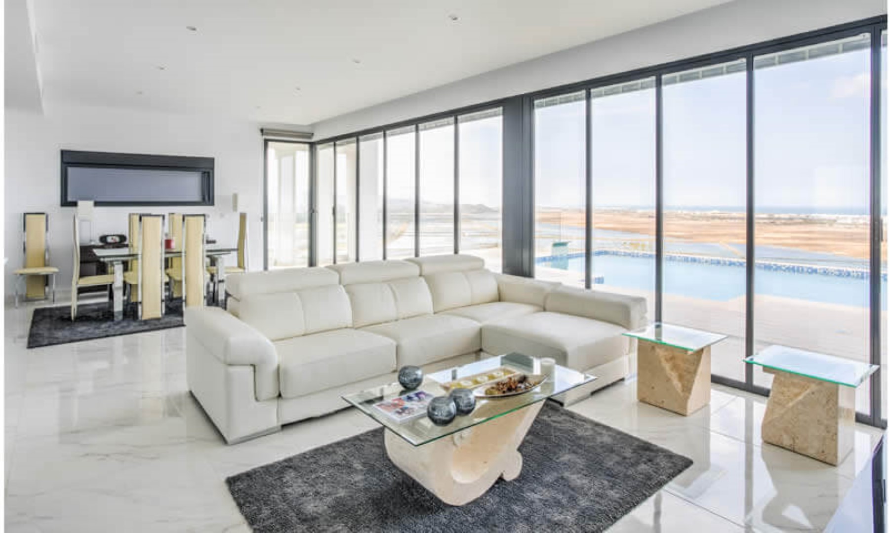 Open-plan living and dining area featuring polished marble floors and floor-to-ceiling glass doors that open onto the infinity pool and panoramic coastal views.