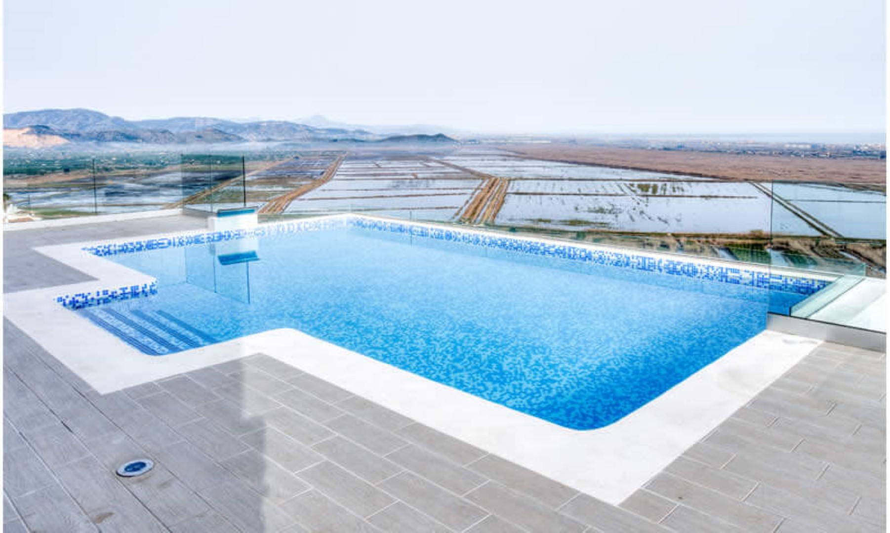 Terrace featuring an infinity pool with blue mosaic tiles and glass safety railings, offering panoramic views of the valley and mountains.