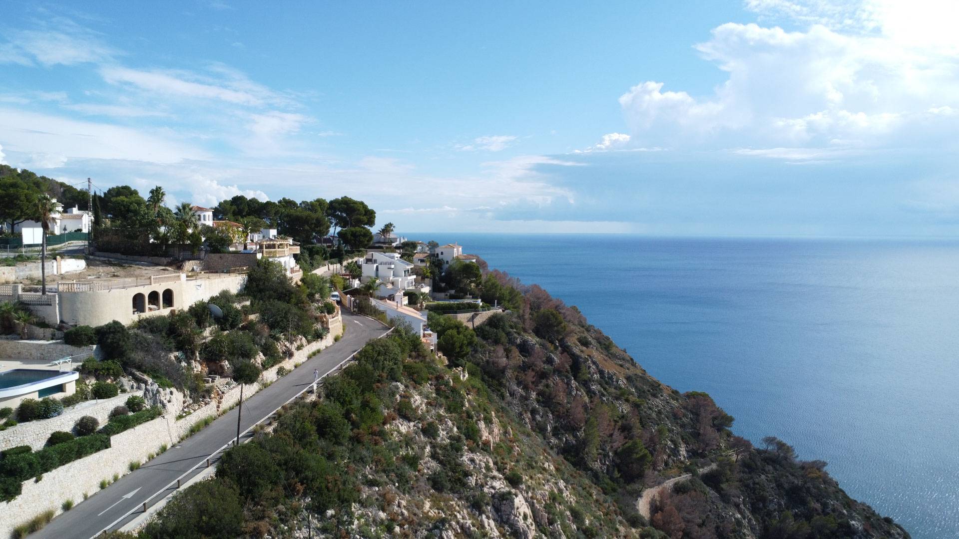 Aerial view of the coastal landscape in La Granadella, featuring the access road and villas nestled into the cliffside overlooking the Mediterranean Sea.
