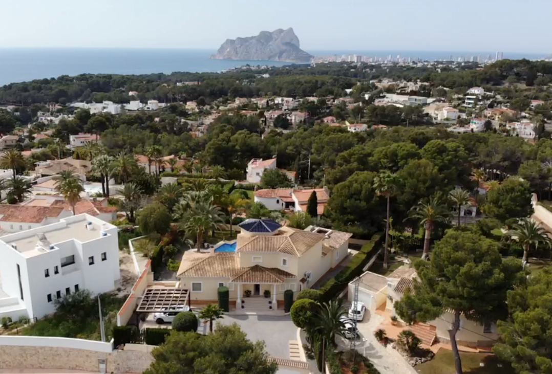 Aerial perspective of the villa showcasing its traditional tiled roof, blue turret, and mature Mediterranean gardens with views of the Peñón de Ifach.