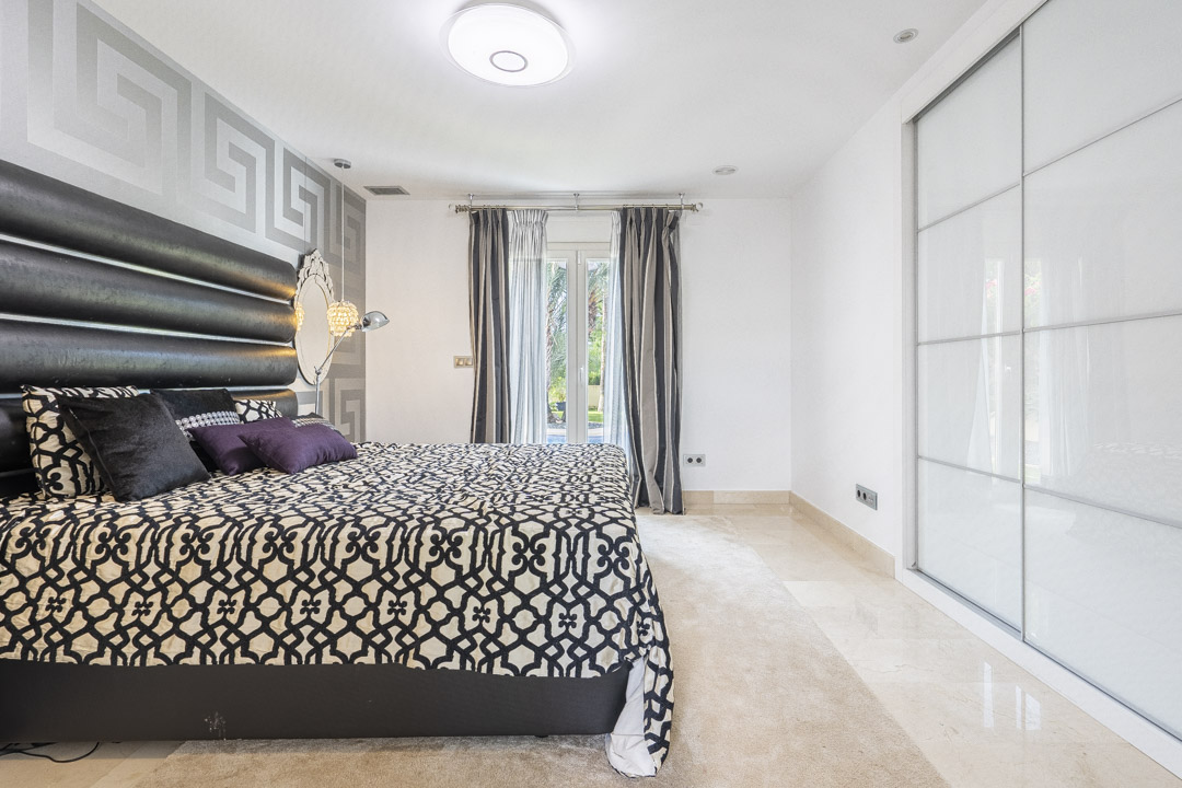 Bedroom featuring a large built-in wardrobe with white sliding doors, polished stone flooring, and direct access to the garden through French doors.