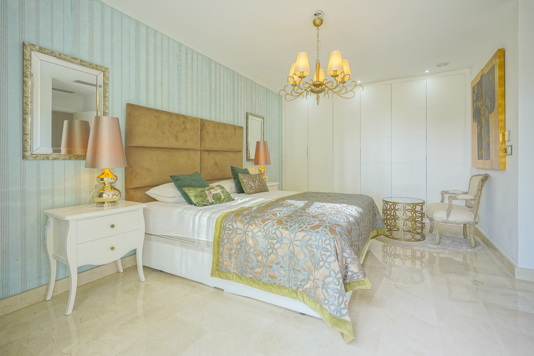 Bedroom featuring blue striped wallpaper, a tan padded headboard, polished marble flooring, and integrated white floor-to-ceiling wardrobes.