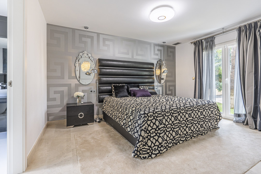 Bedroom featuring Greek key wallpaper, a black tufted headboard, and large glass doors offering direct access to the landscaped garden.
