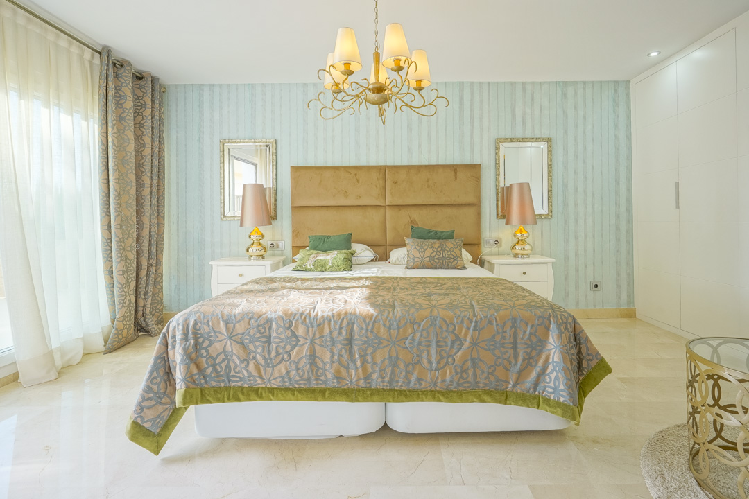 Elegant bedroom featuring turquoise striped wallpaper, a mustard velvet headboard, and polished marble floors. Includes white built-in wardrobes and ample natural light.