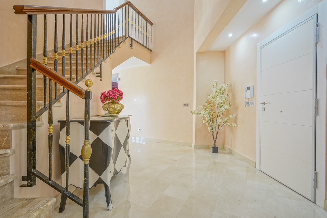 Entrance hall featuring polished marble floors, a stone staircase with wrought iron railings, and a decorative harlequin-patterned sideboard.