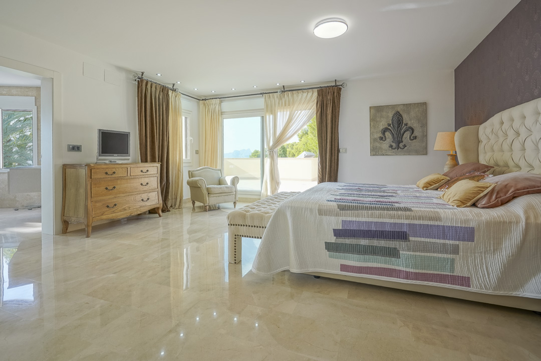 Master bedroom featuring polished marble flooring, a tufted headboard, and sliding glass doors opening onto a terrace with views of the Peñón de Ifach.