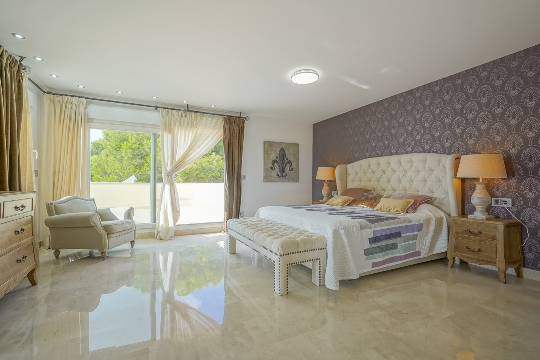 Master bedroom featuring polished stone floors, a patterned accent wall, and large sliding doors opening onto a private sun terrace.
