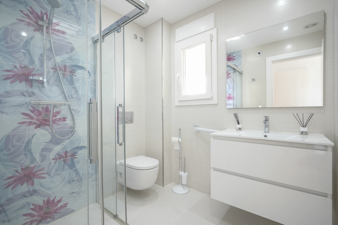 Modern bathroom featuring a glass-enclosed shower with floral accent tiles, a floating white vanity, and wall-mounted fixtures in a neutral palette.
