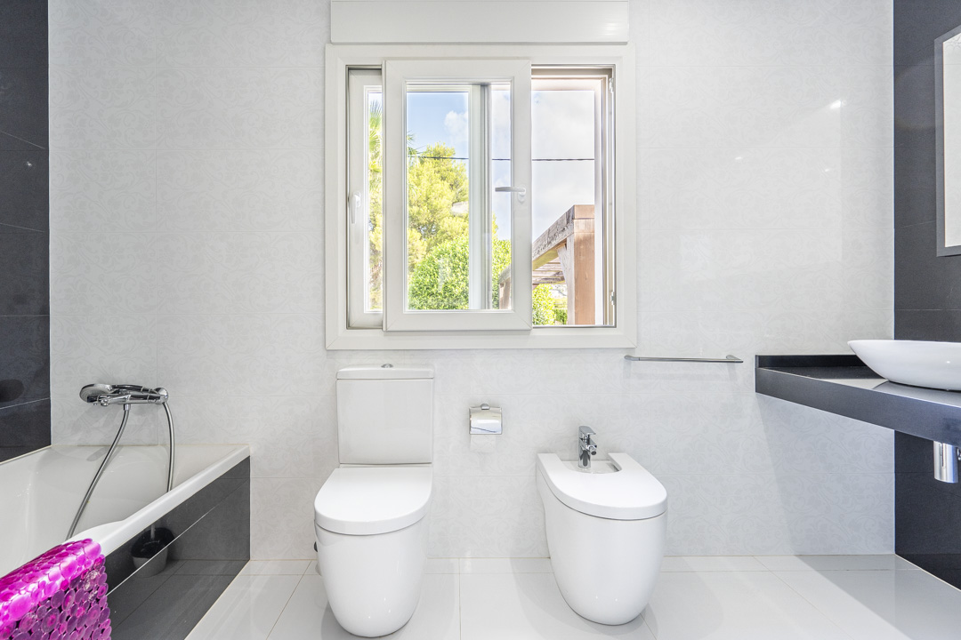 Modern bathroom featuring a white toilet, bidet, and bathtub with black panels. It includes a floating black vanity with a vessel sink and a window overlooking the garden.