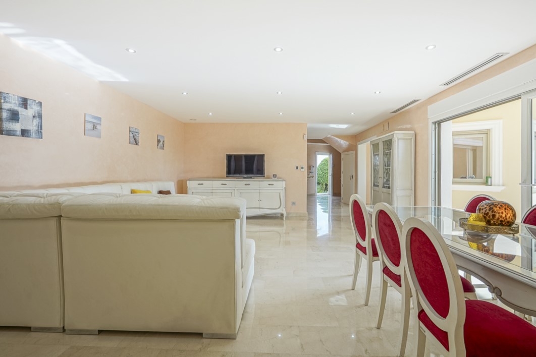 Open-plan living and dining area featuring polished marble flooring, recessed ceiling lighting, and large sliding glass doors leading to the terrace.
