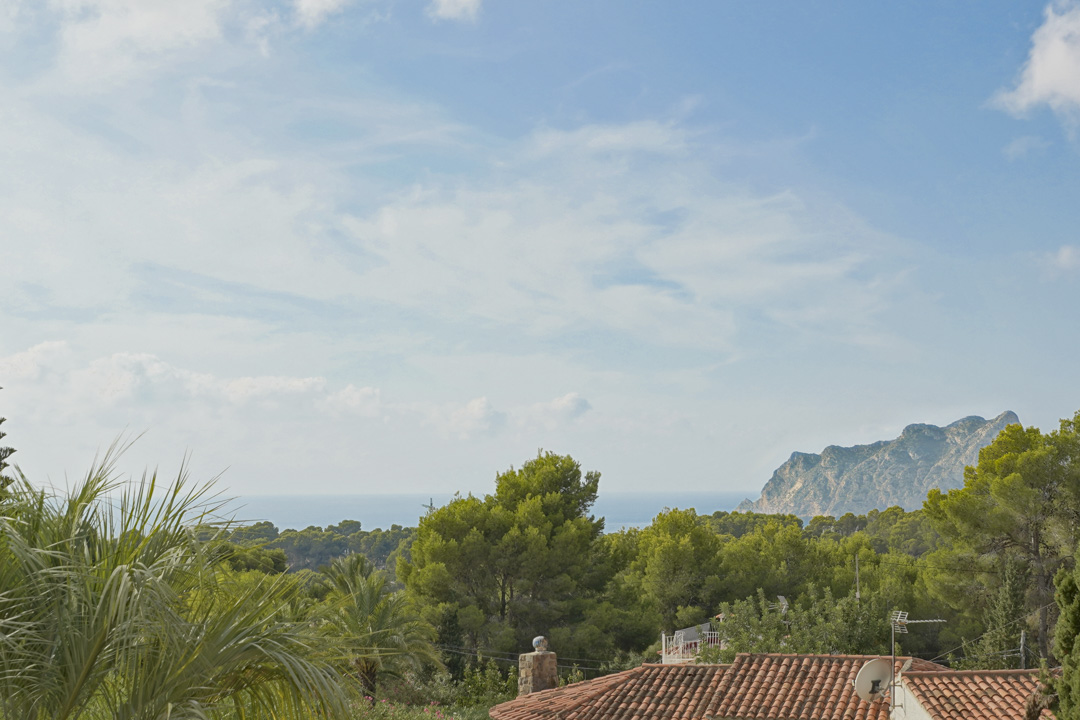Panoramic views of the Mediterranean Sea and the Peñón de Ifach from the upper level, framed by lush pine trees and local vegetation.