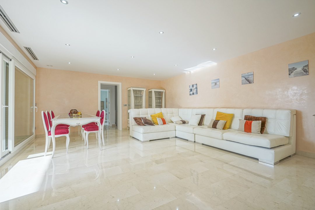 Spacious living-dining area featuring polished marble floors, a large white leather sectional sofa, and direct terrace access through sliding glass doors.