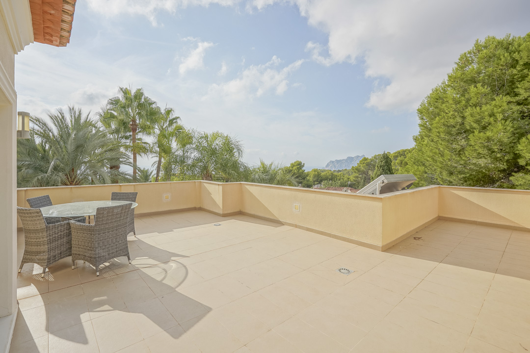 Spacious upper terrace featuring tiled flooring and outdoor dining furniture, with panoramic views of the Peñón de Ifach and mature palm trees.