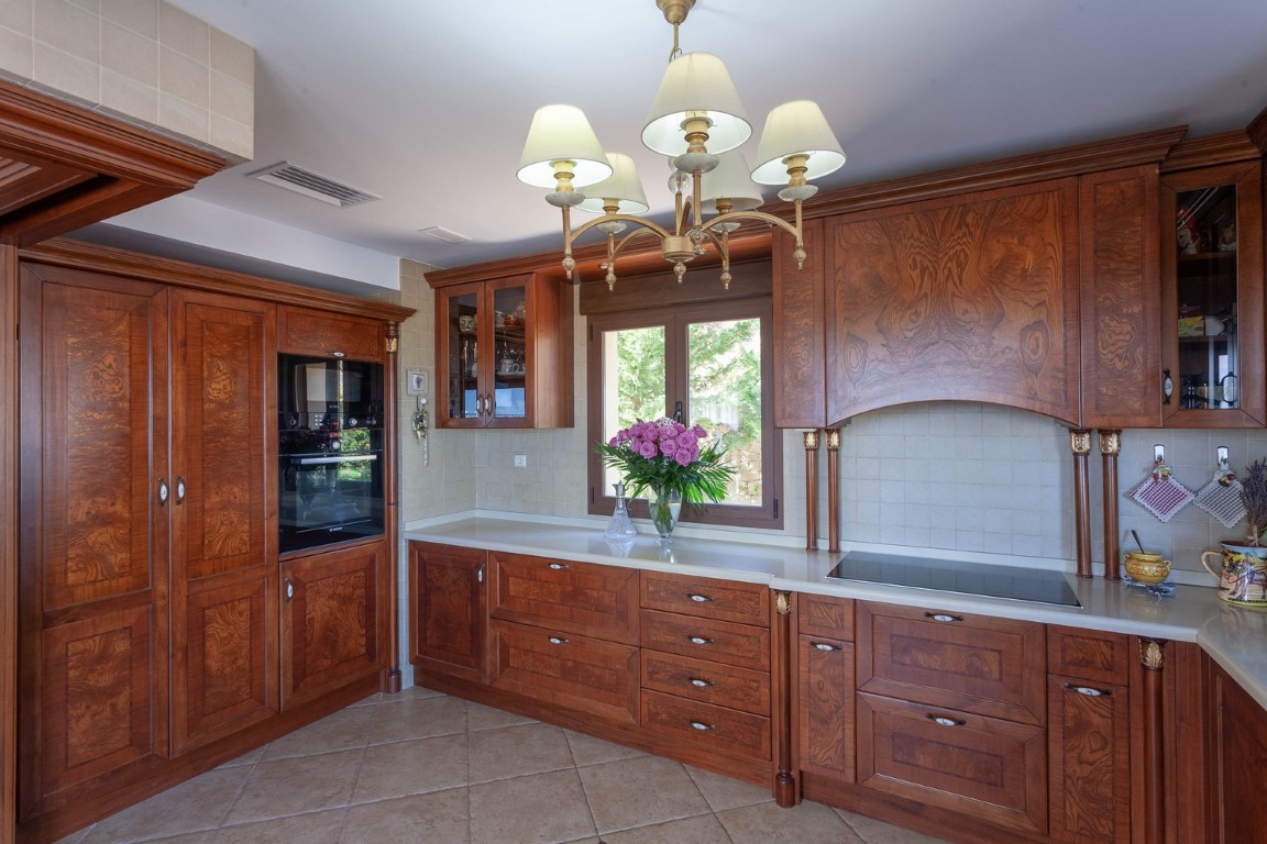 Classic kitchen featuring ornate wood cabinetry, white countertops, and integrated appliances. The space includes an induction hob and a traditional tiered chandelier.
