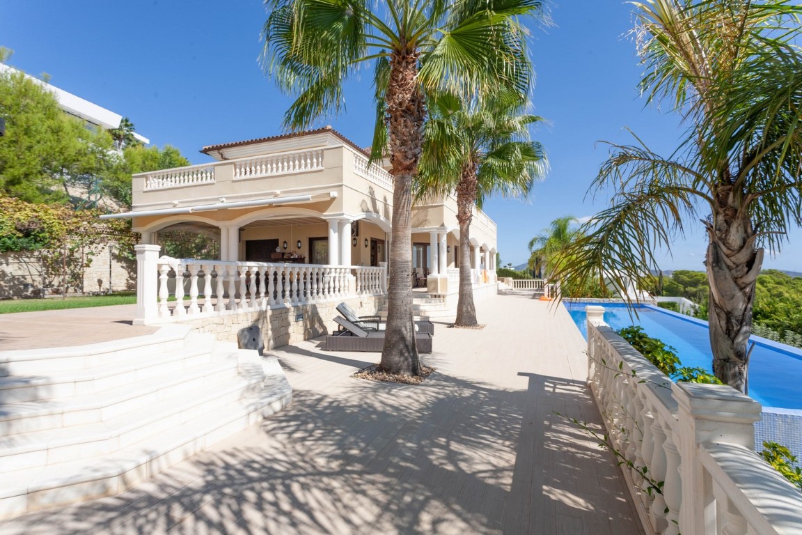 Exterior terrace featuring classic balustrades, palm trees, and a long infinity pool adjacent to the Mediterranean villa with arched porches.