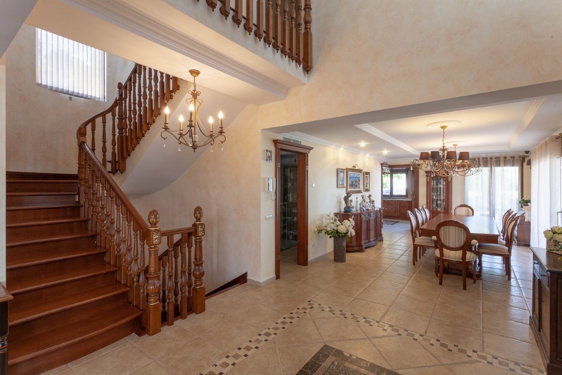 Spacious entrance hall featuring a carved wooden staircase and decorative tiled flooring, leading into a formal dining area with classic furnishings.